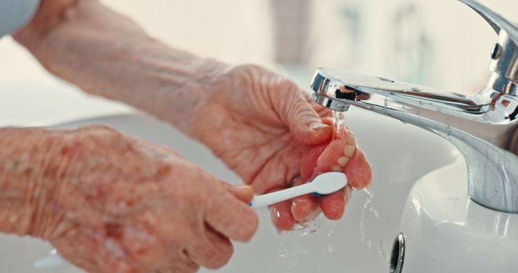 Elderly person washing dentures under a running tap