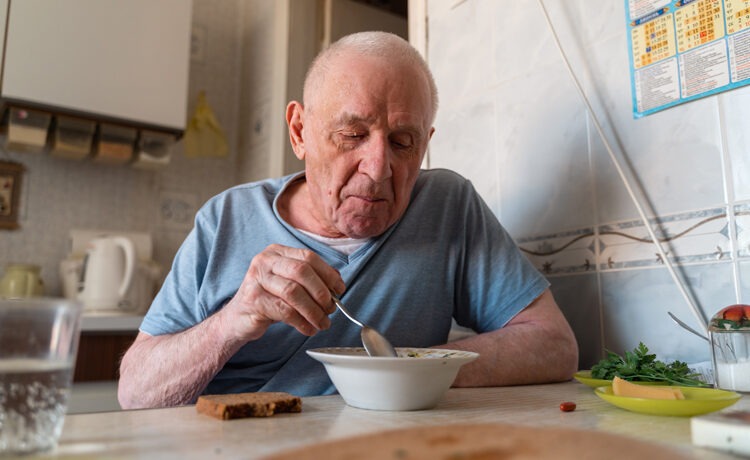Elderly man eating soup with some bread