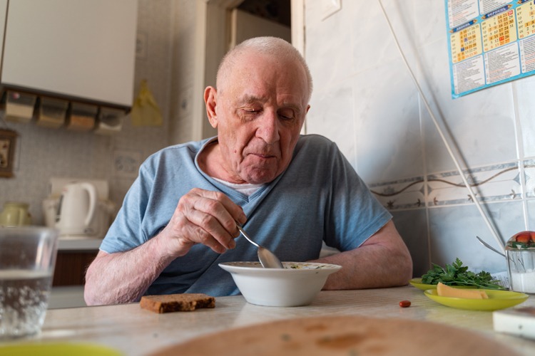 Elderly man eating soup with some bread