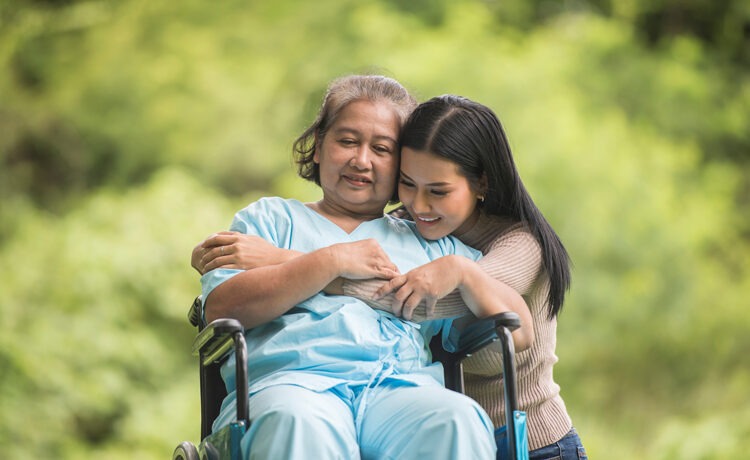 An elderly woman in a wheelchair being hugged by a young woman.