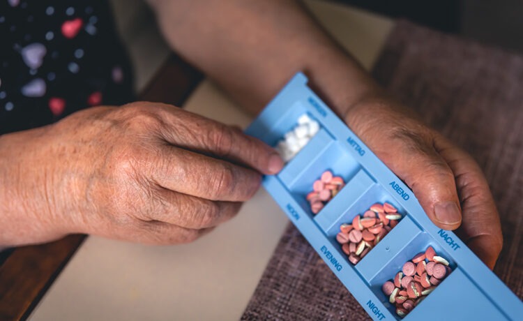 An elderly woman reviewing her pills in a blue container