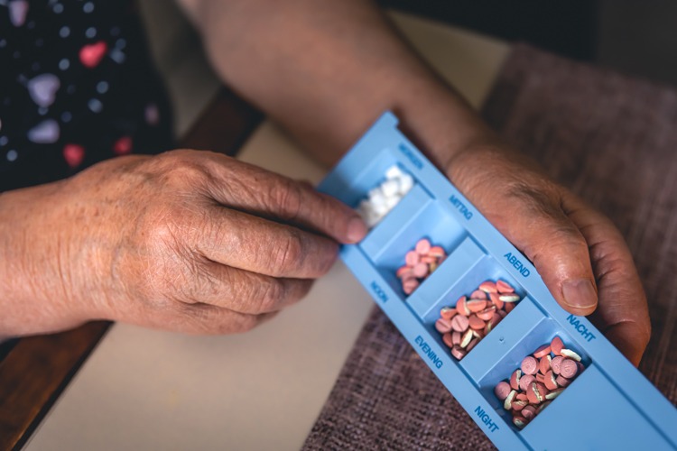 An elderly woman reviewing her pills in a blue container